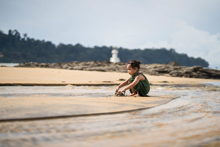 Girl sitting on shore at beach against sky