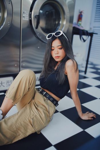 Young woman sitting on floor against washing machine