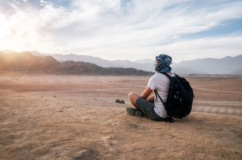 Man sitting on sand against landscape and sky