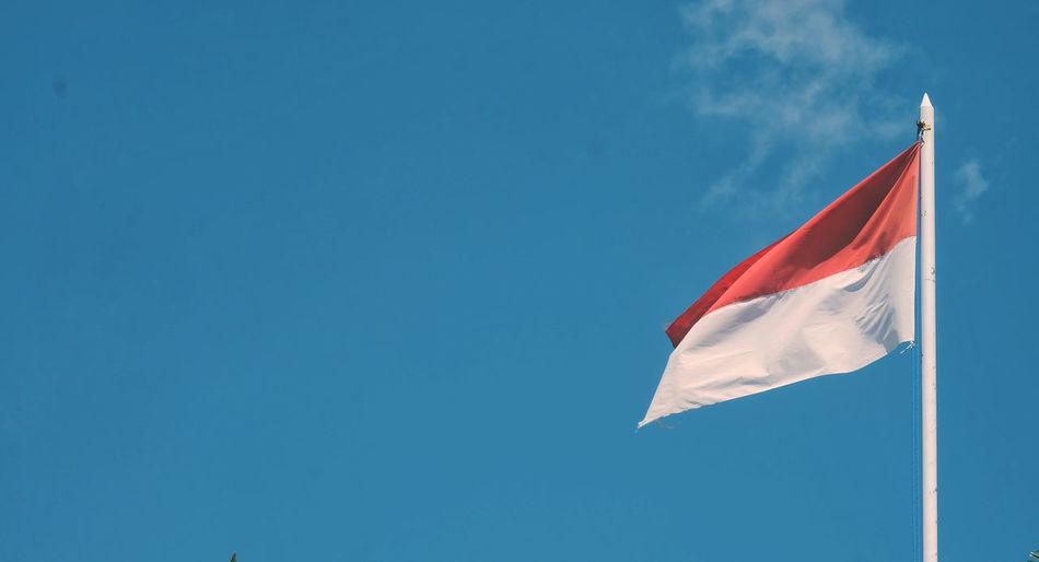 Low angle view of indonesian flag waving against blue sky
