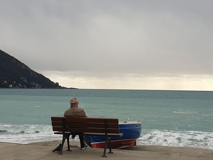 Rear view of man sitting on bench at beach