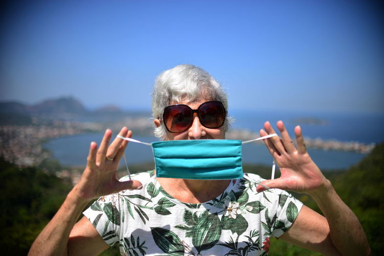 Portrait of elderly woman wearing sunglasses against sky showing mask