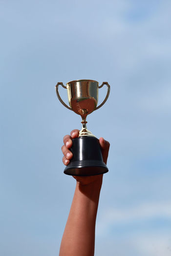Cropped hand of woman holding trophy against sky