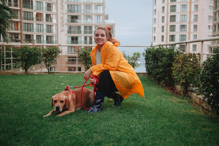 Caucasian smiling girl in yellow rain coat sitting with a dog on the grass. people in fall concept