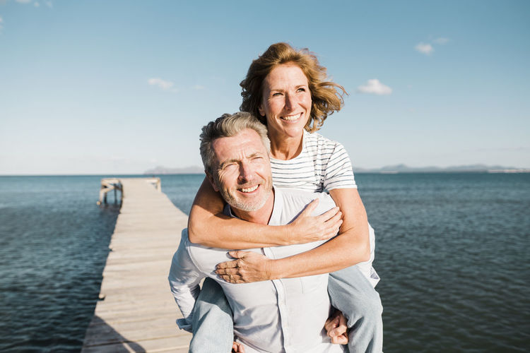 Happy man giving piggyback ride to woman on jetty