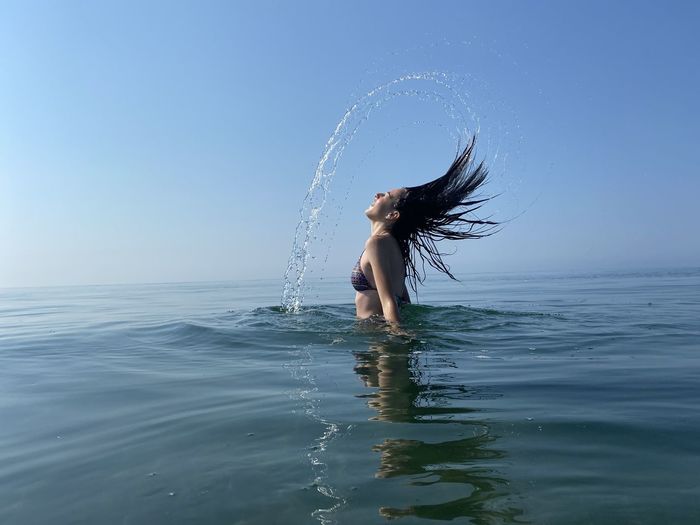 Side view of girl splashing water in sea against sky