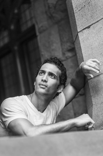 Portrait of young man standing by rock window, looking up.