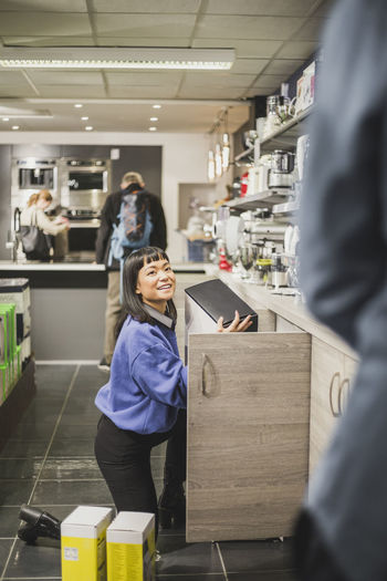 Smiling saleswoman with appliance looking at coworker in store