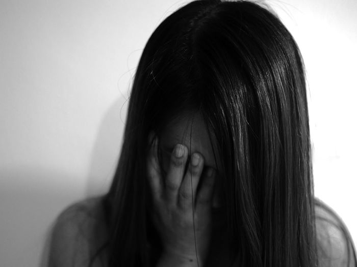 Close-up of depressed woman covering eyes against wall