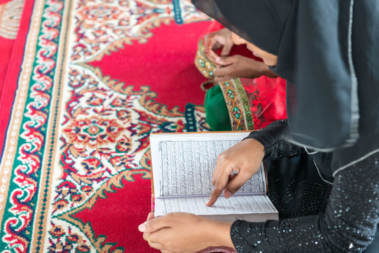 Woman reading koran while sitting on carpet
