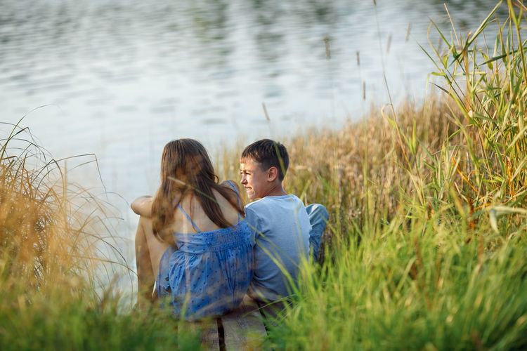 Rear view of couple sitting on grass by lake