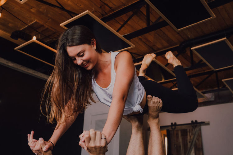 High angle side view of happy young barefooted couple in activewear looking at each other and smiling while doing balance exercise standing in front plank position on floor in contemporary studio