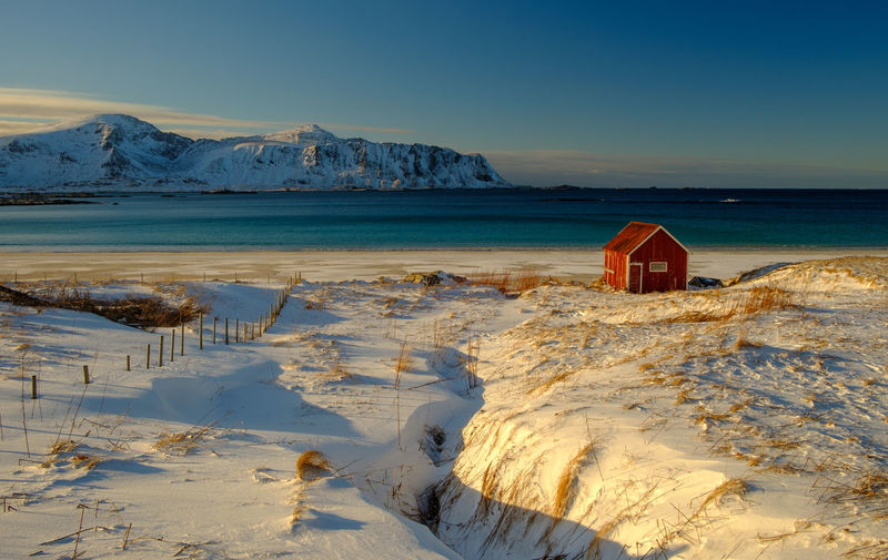 Red log cabin on snow covered landscape against sea