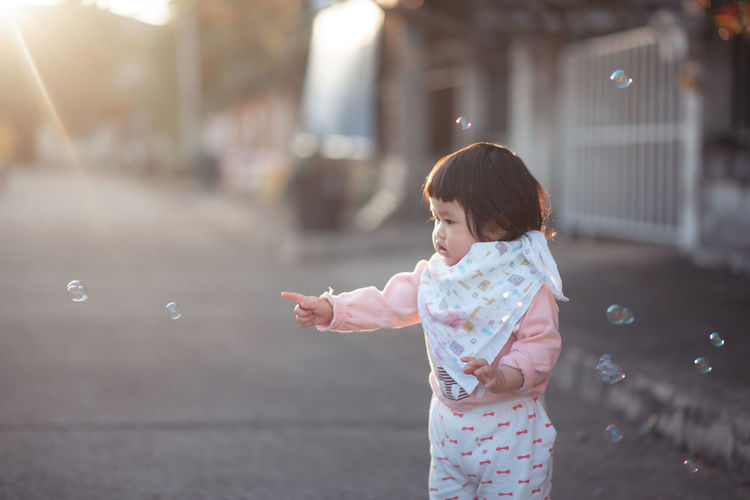 Cute girl looking at bubbles while standing on road