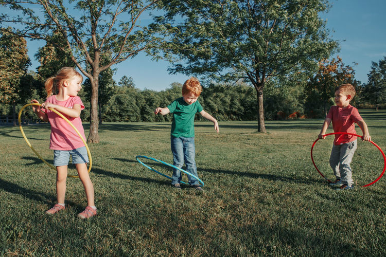 Full length of children playing with plastic hoops on grassy land in park
