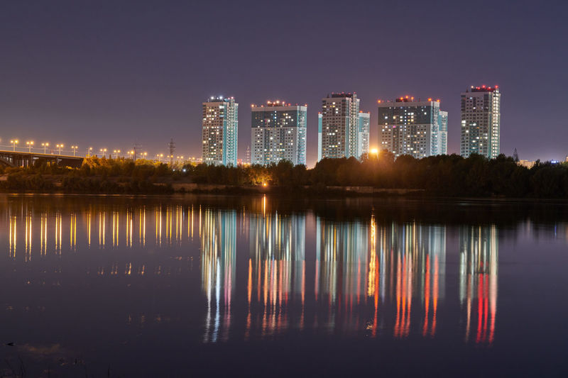 Illuminated buildings by lake against clear sky at night