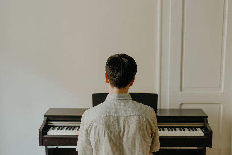 Rear view of boy playing piano against wall