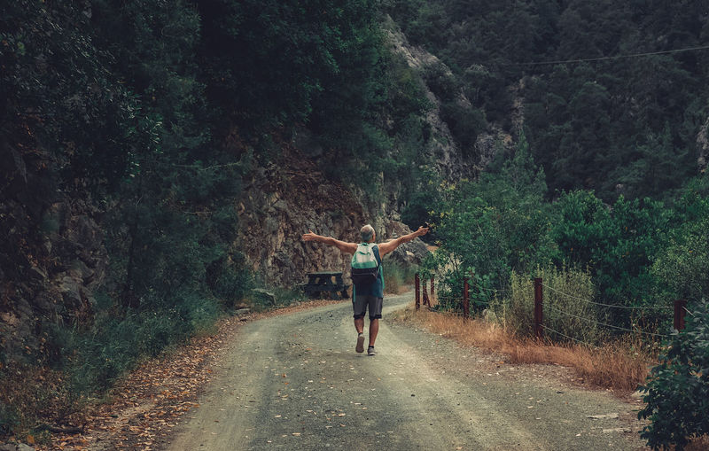 Senior man in the middle of the road in the forrest. hiker in the nature with hands open.