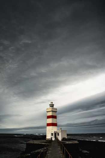 Lighthouse by sea against dramatic sky