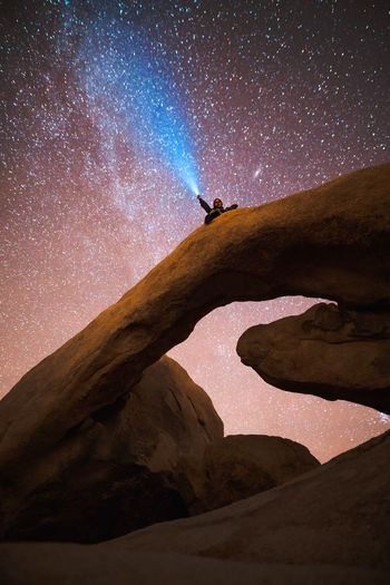Low angle view of man sitting on natural arch against starry sky at night