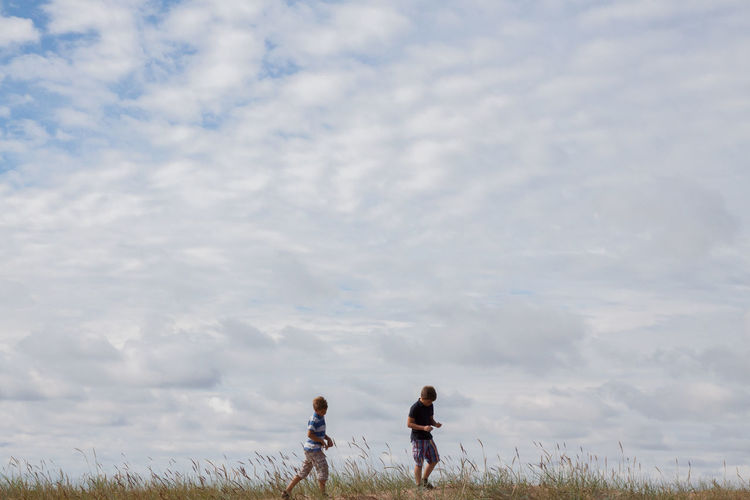 Friends walking on field against cloudy sky