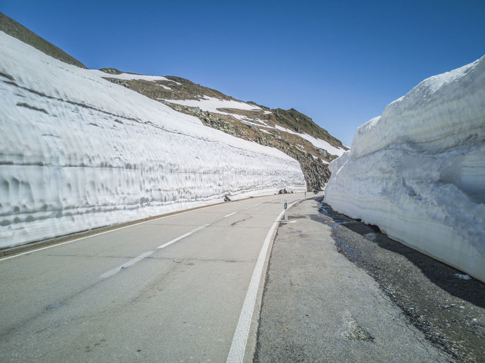 Road amidst snowcapped mountains against clear sky