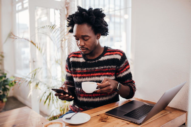 Technology One Person Wireless Technology Connection Computer Communication Laptop Young Adult Cup Real People Sitting Coffee Table Food And Drink Coffee - Drink Indoors Coffee Cup Using Laptop Drink