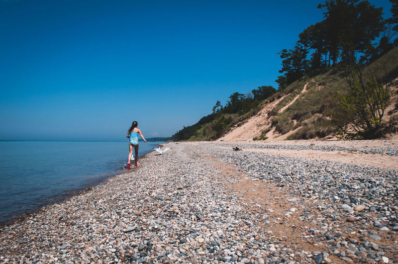 Girl walking on shore against clear blue sky
