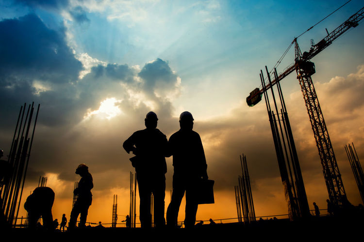 Silhouette workers working at construction site against cloudy sky during sunset