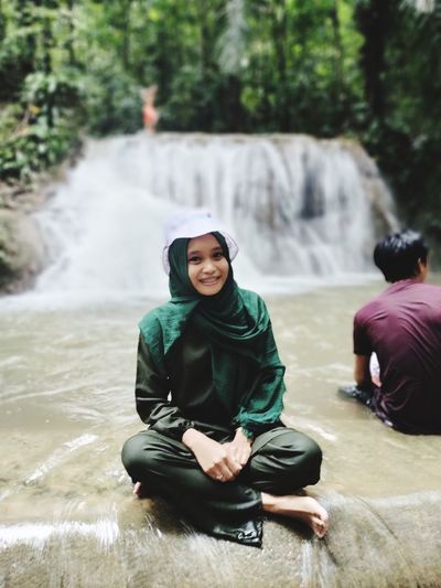 Portrait of a smiling woman sitting against waterfall