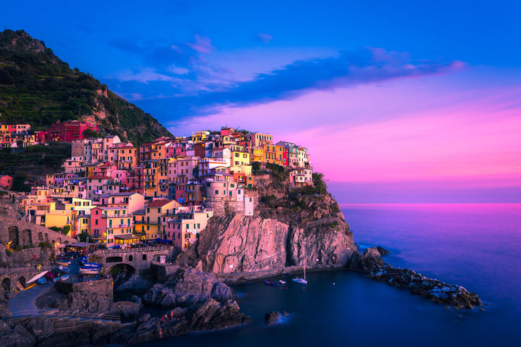 Houses on mountain by sea against sky at sunset