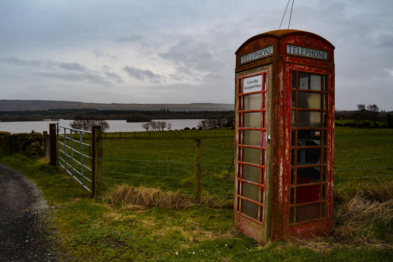 Old telephone booth on field against sky