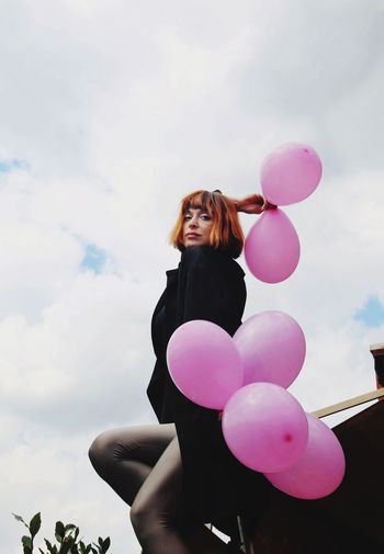 Low angle view of woman with pink balloons against sky