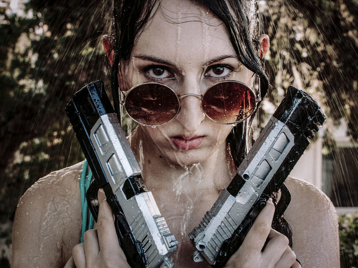 Portrait of woman holding guns under falling water