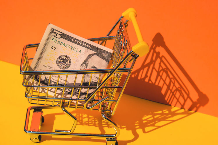 Close-up of miniature shopping cart against yellow background