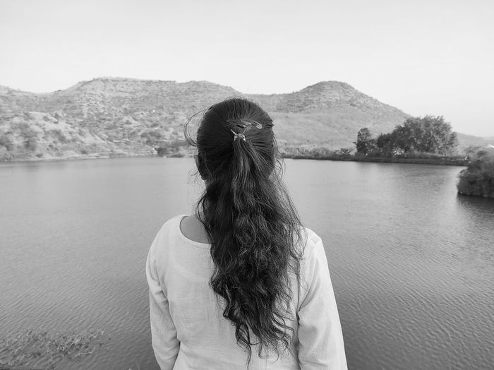 Rear view of woman standing by lake against mountain