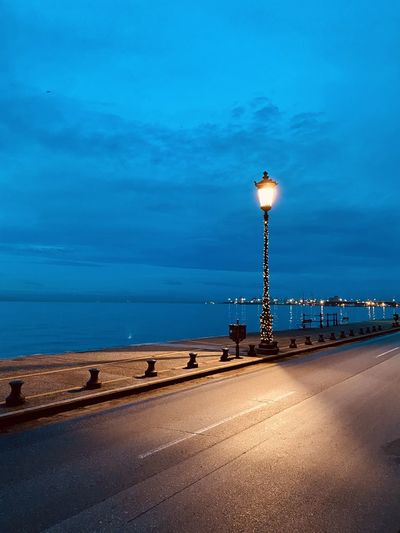 Street light on road by sea against blue sky