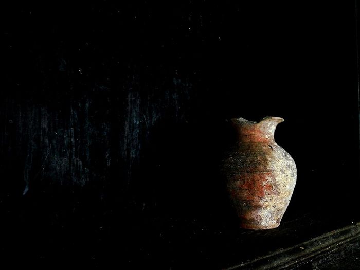 Close-up of old vase on table against black background