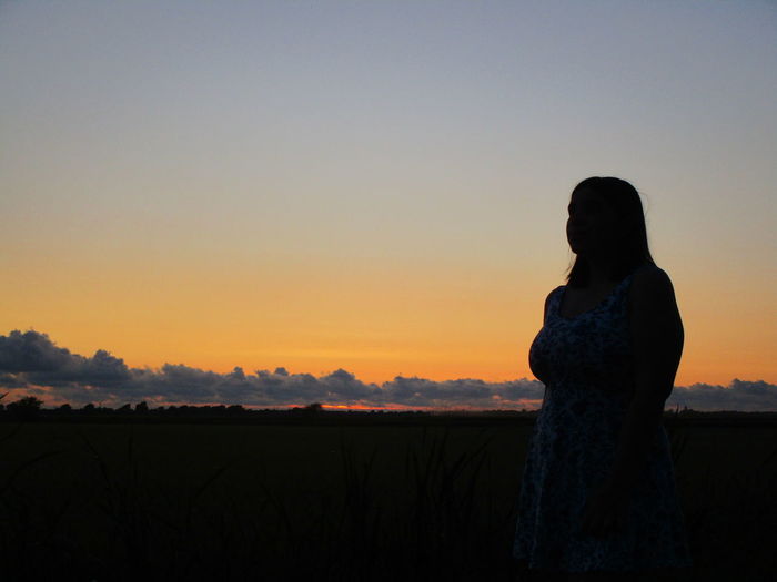 Silhouette teenage girl standing on field against sky during sunset