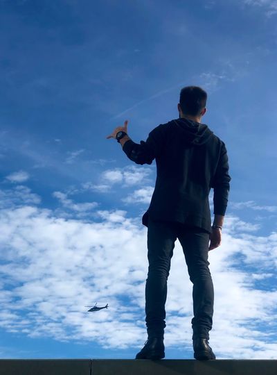 Rear view of man gesturing shaka sign while standing against sky