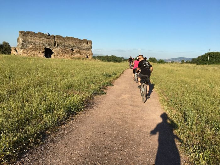 Rear view of cyclist on dirt road against blue sky