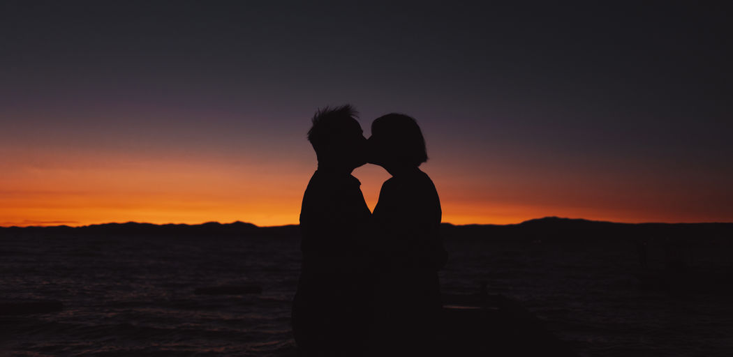 Couple of lovers kissing with sunset beach on the background - focus on people silhouette