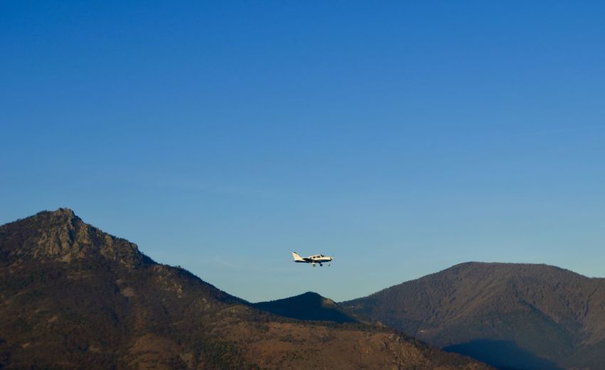 Low angle view of airplane flying over mountains against blue sky