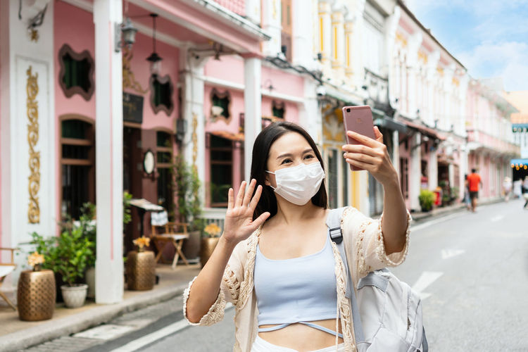 Smiling woman wearing mask talking on video call on street