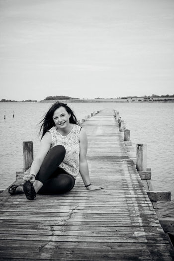 Portrait of young woman sitting on jetty over lake
