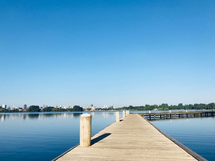 Pier over lake against clear blue sky