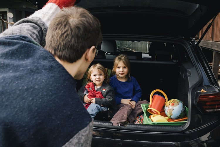 Father talking to daughters sitting in electric car trunk