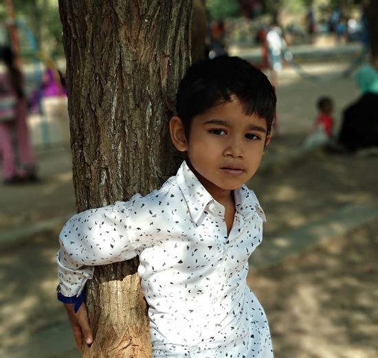 Portrait of cute boy against tree trunk