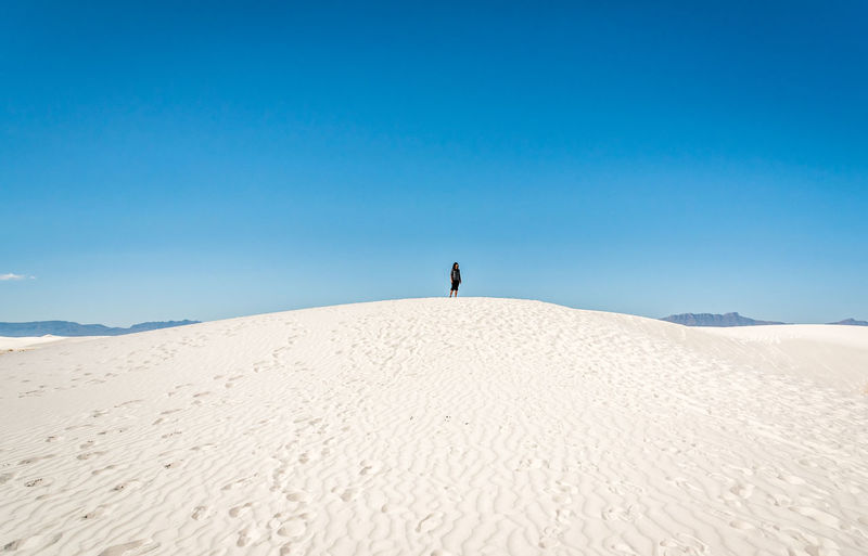 Woman standing on sand against blue sky at desert