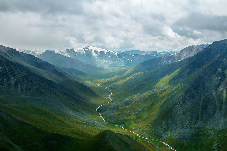 Green mountain gorge in summer with river, snow-capped peaks in the distance, sky with clouds